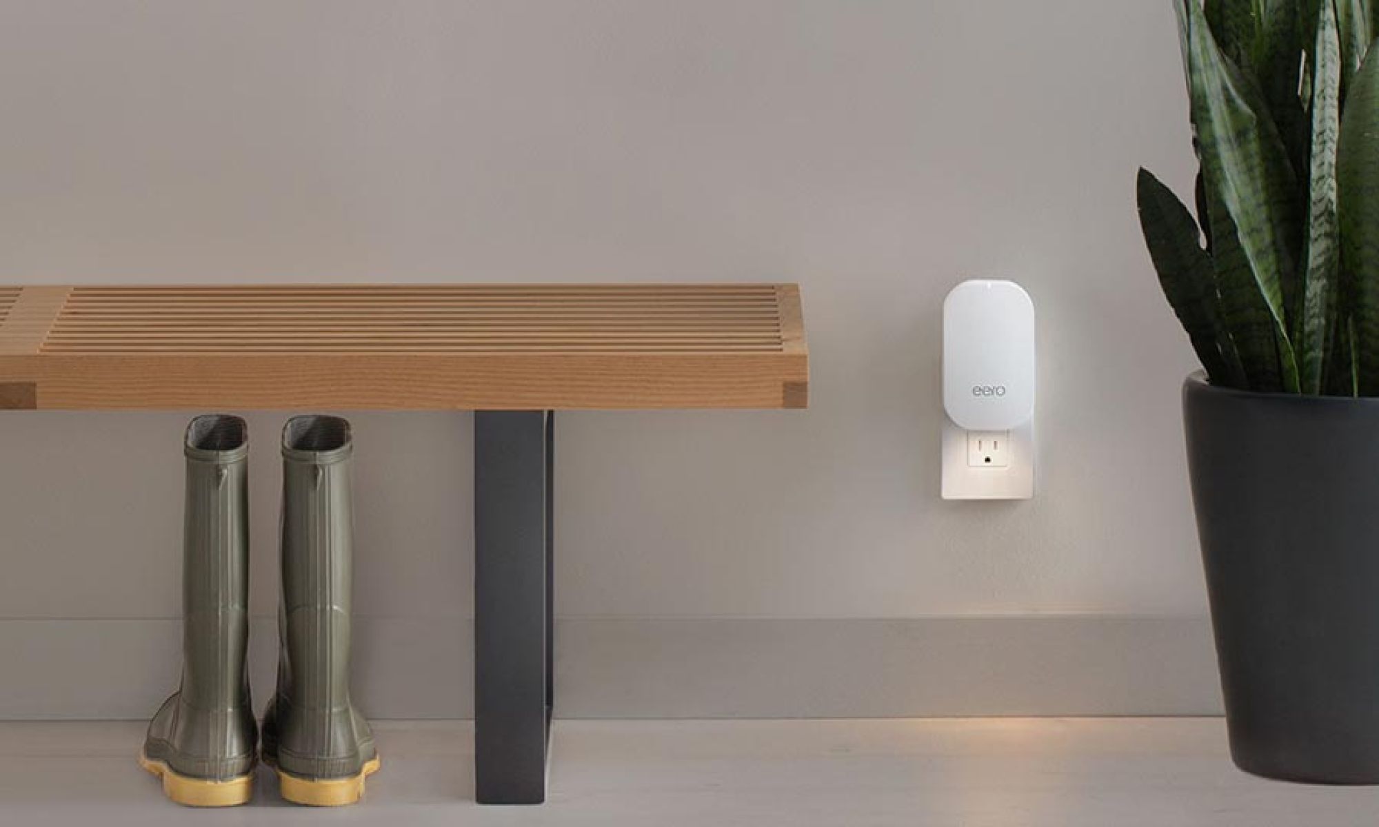 A minimalist interior with a white eero Wi-Fi extender plugged into the wall next to a bench and a potted plant.