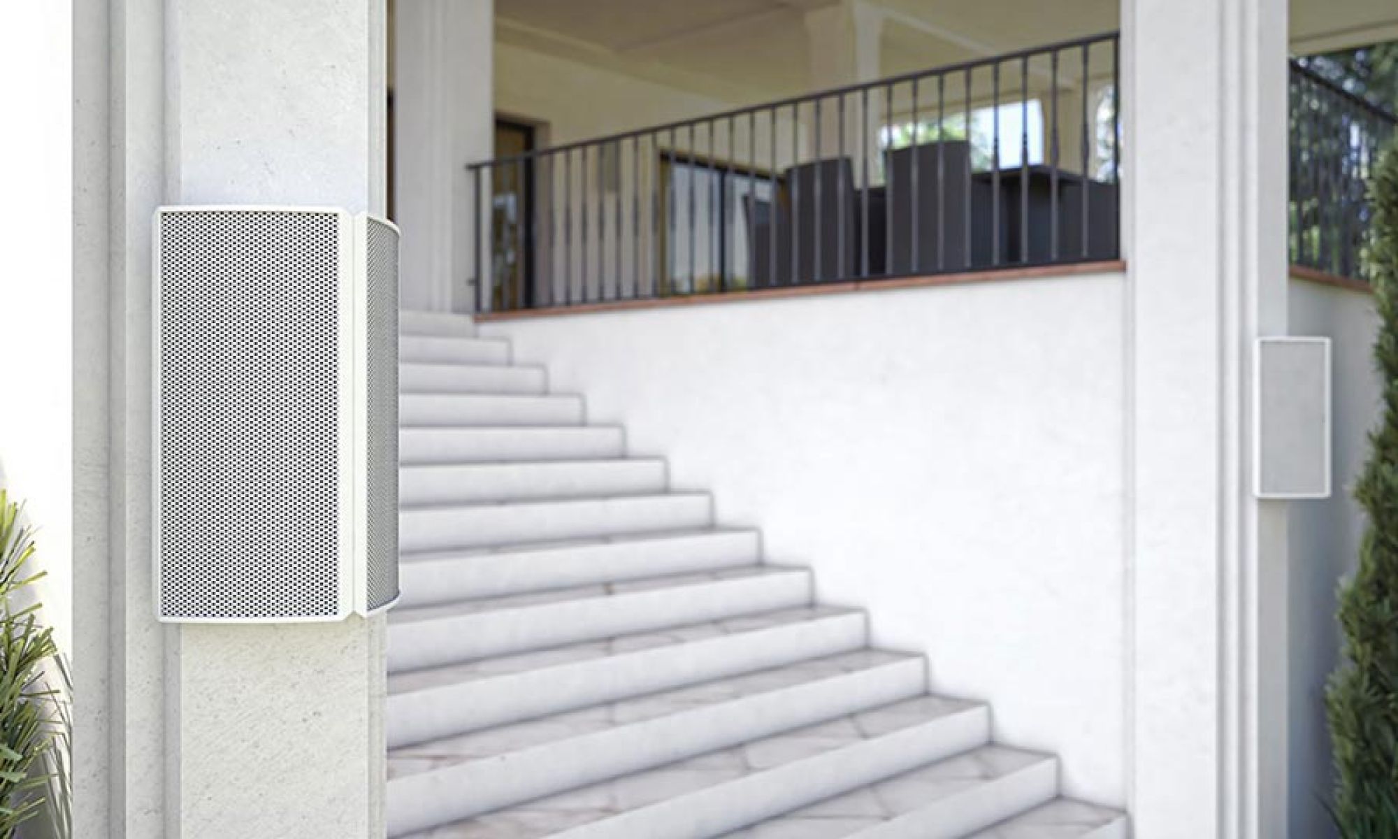 An outdoor patio with white weather-resistant speakers mounted on pillars near a staircase, leading up to a covered seating area. Source