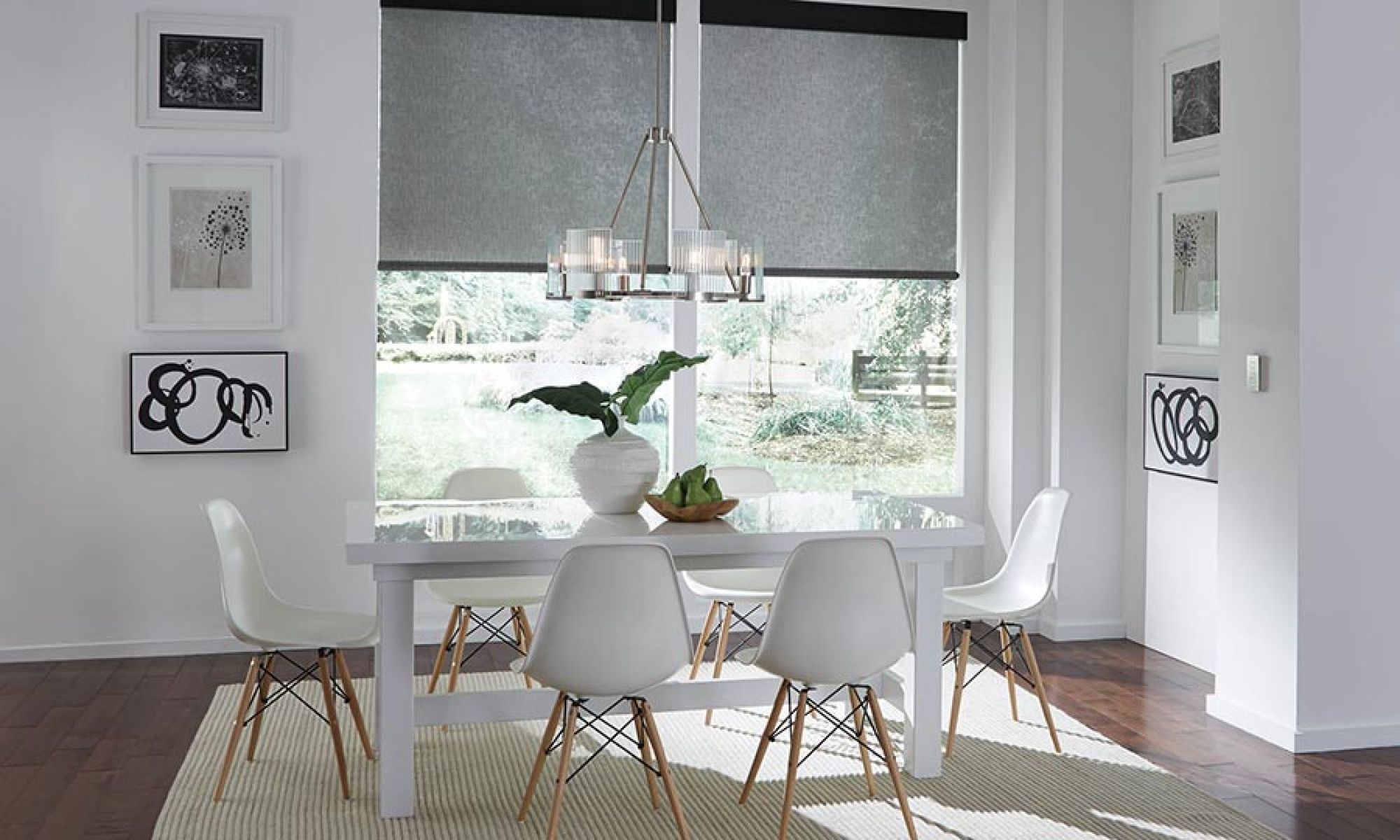 A bright dining room with large windows covered by automated shades, contemporary furniture, and elegant lighting.