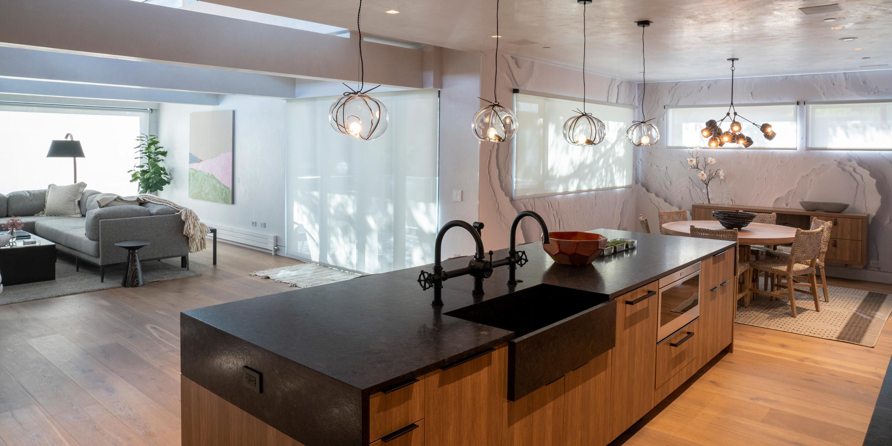 An open-plan kitchen with a large island, dark countertops, and pendant lighting, leading into a spacious living and dining area.