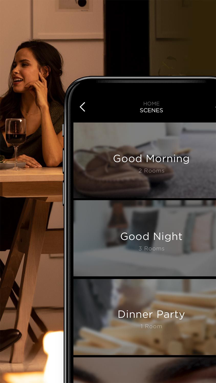 A woman enjoys wine while an app on a smartphone displays home automation scenes for different moods and times of day.