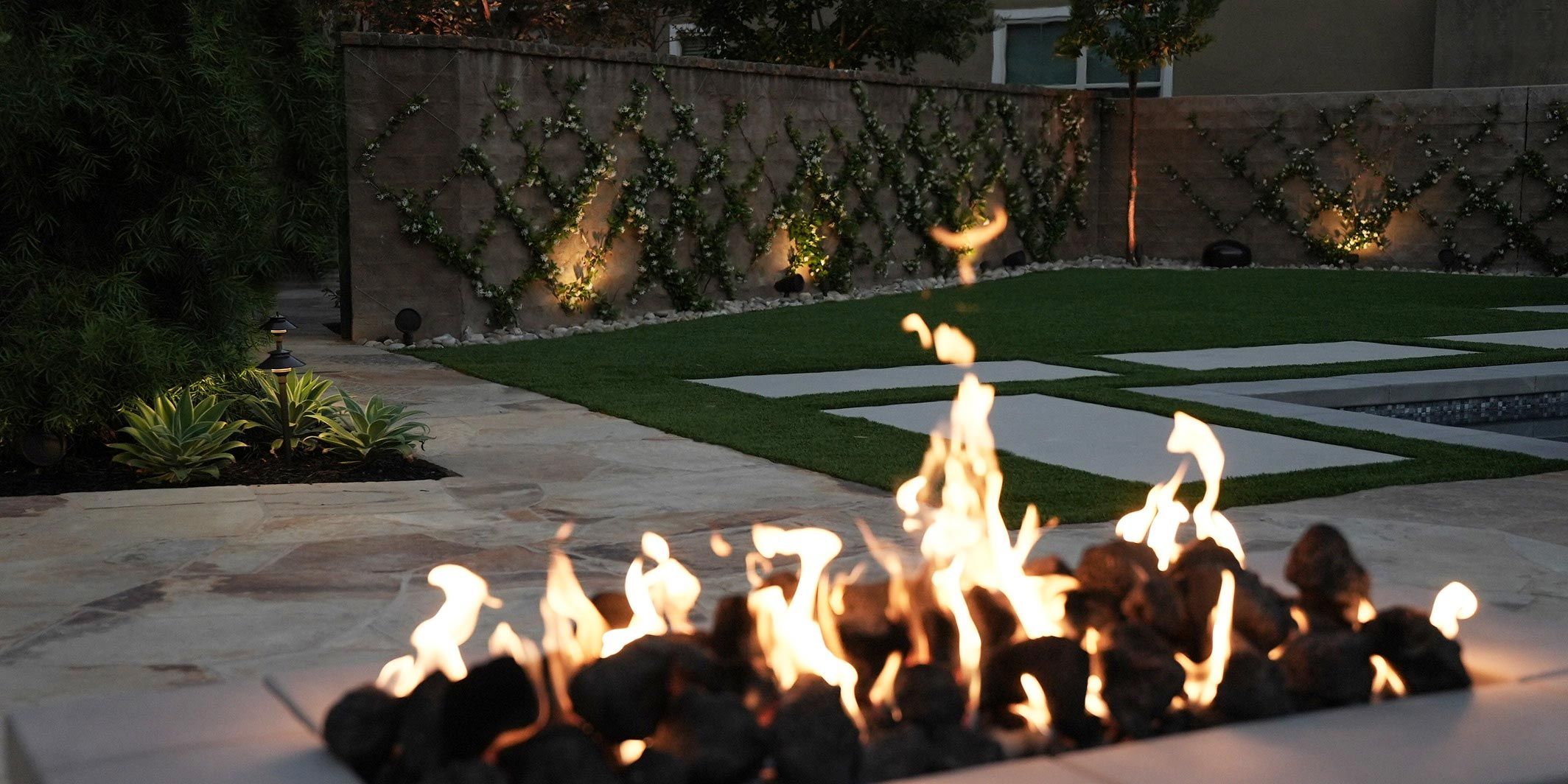 A cozy outdoor garden with a fire feature, stone pathways, and subtle lighting, creating a peaceful evening ambiance.