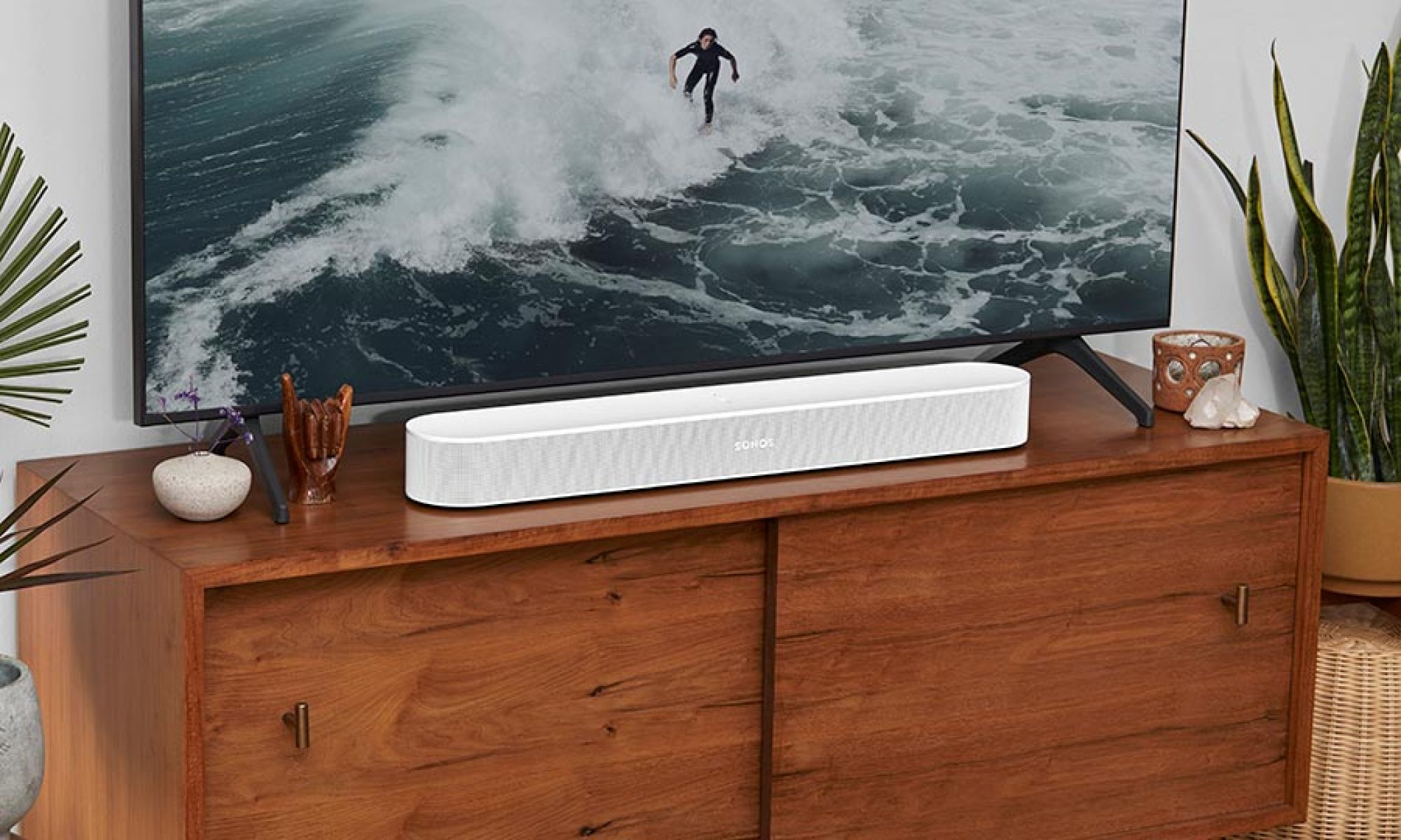 A living room featuring a white soundbar on a wooden console beneath a television displaying a surfer in the ocean.